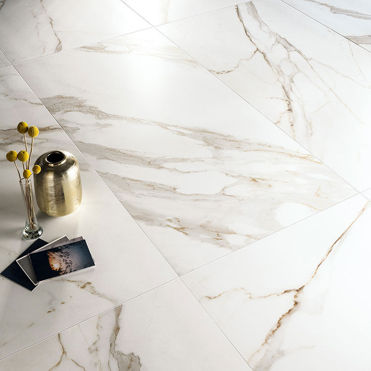 Immagine ravvicinata di un pavimento della collezione "Charme", effetto marmo Gold con alcuni oggetti posati su di esso e un riflesso di luce
