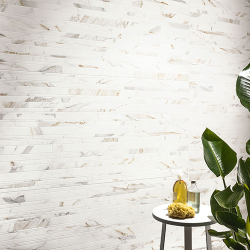 Particolare ravvicinato del rivestimento di un bagno, serie Charme colore Gold, con una pianta e uno sgabello con portasapone