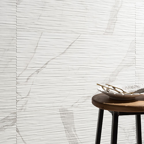 Immagine ravvicinata del rivestimento serie Charme colore Veined, con uno sgabello ed alcune posate poste davanti al rivestimento in gres con effetto marmo bianco e venature scure