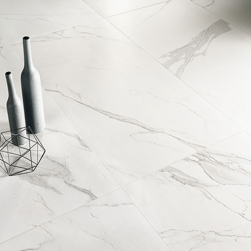 Immagine ravvicinata del pavimento serie Charme colore Veined, con due bottiglie posate sul pavimento in gres con effetto marmo bianco e venature scure