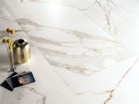 Immagine ravvicinata di un pavimento della collezione "Charme", effetto marmo Gold con alcuni oggetti posati su di esso e un riflesso di luce