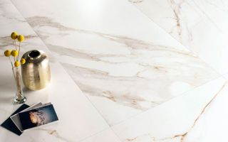 Immagine ravvicinata del pavimento serie Charme colore Gold, con oggetti e fotografie posati su un pavimento in gres con effetto marmo bianco e venature dorate